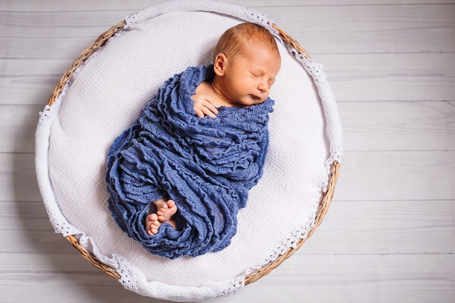 newborn-baby-enveloped-blue-scarf-sleeps-white-pillow